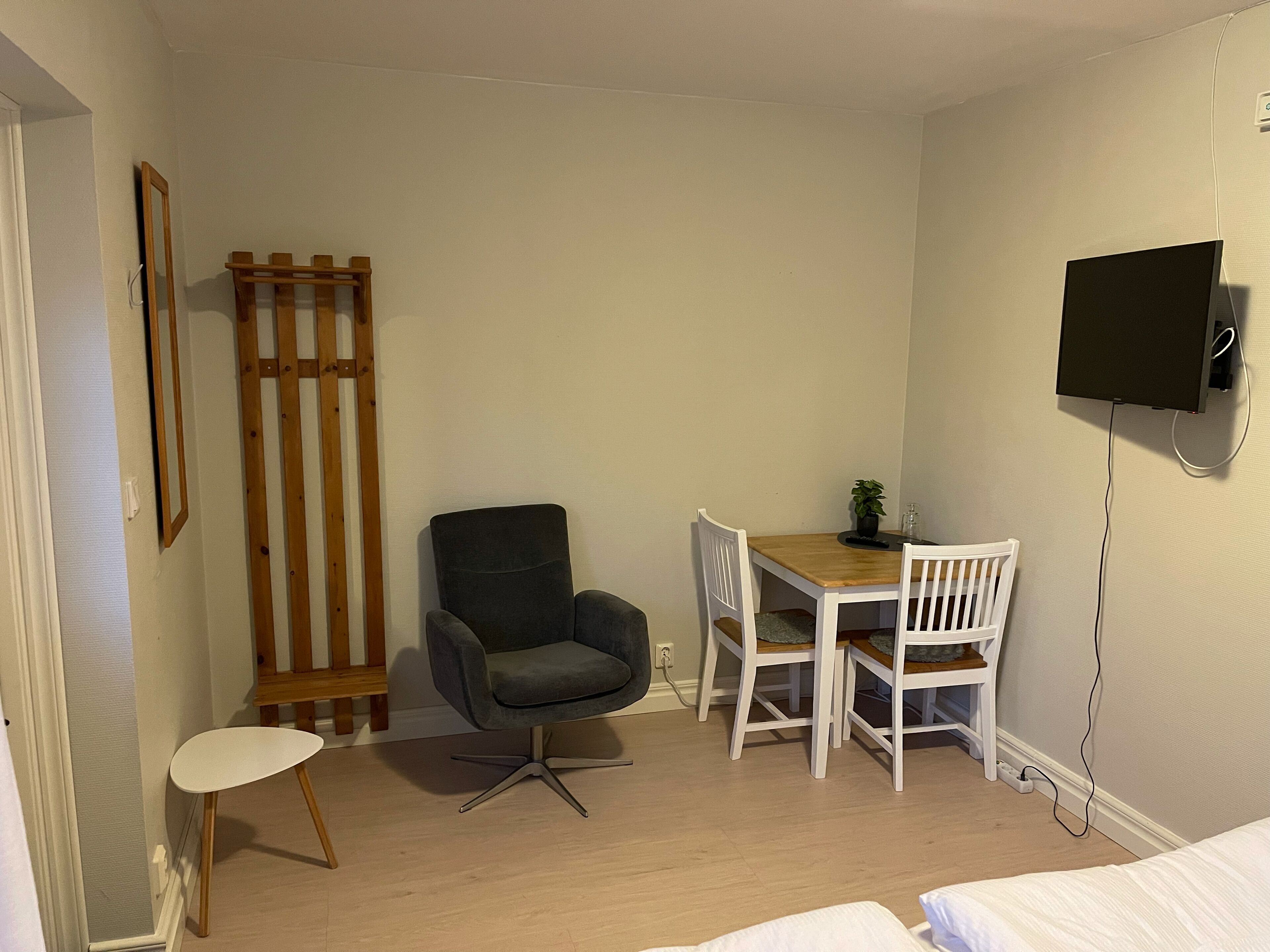 Une petite pièce, bien rangée, avec un lit, un bureau, deux chaises, un téléviseur fixé au mur et une échelle en bois appuyée contre le mur.