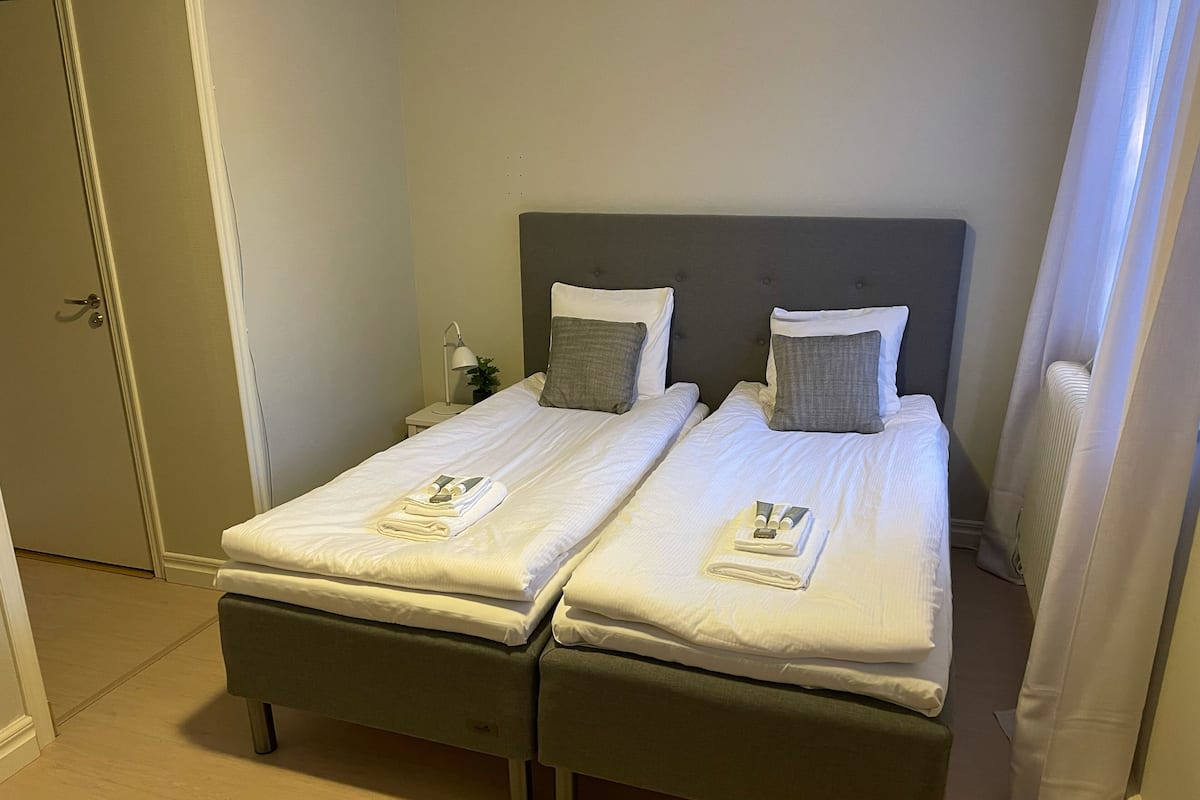 A double bed with a grey headboard, white linens, and a folded towel and toiletries on the bed.