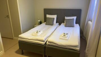 A double bed with a grey headboard, white linens, and a folded towel and toiletries on the bed.