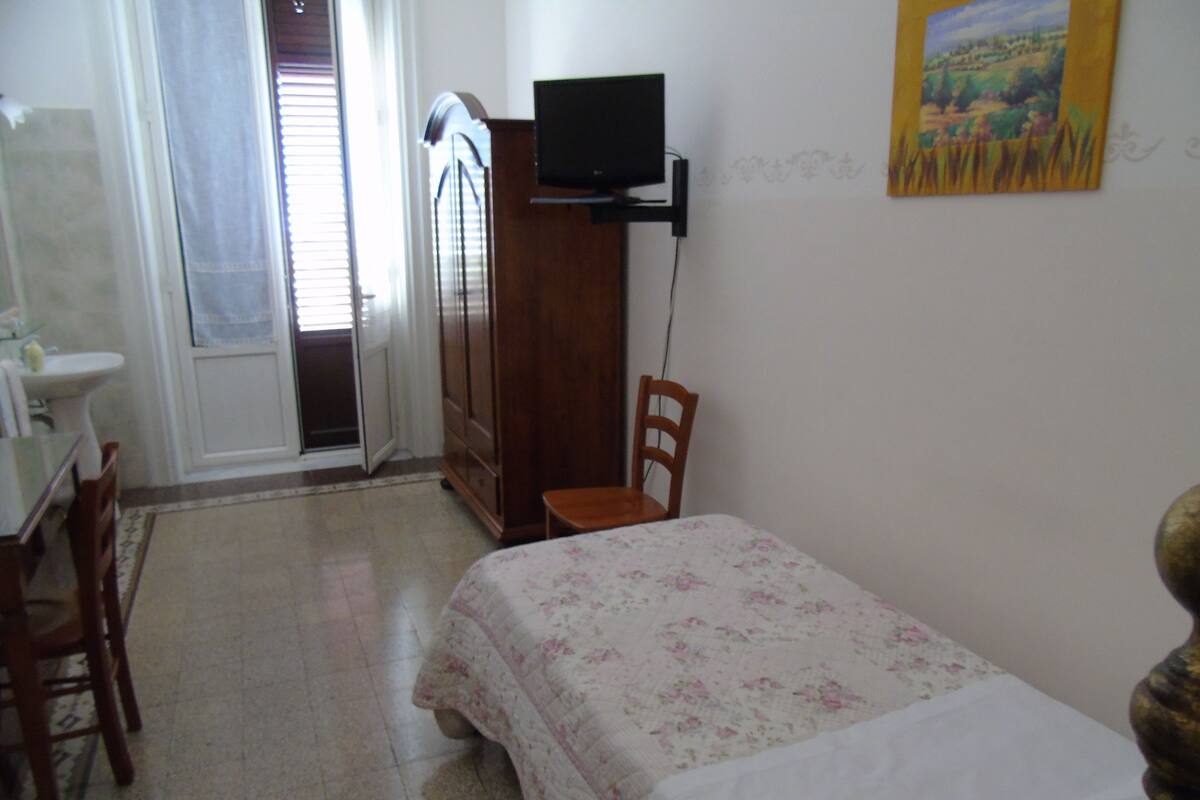A bedroom with a bed, a chair, a desk, a television, and a painting on the wall.