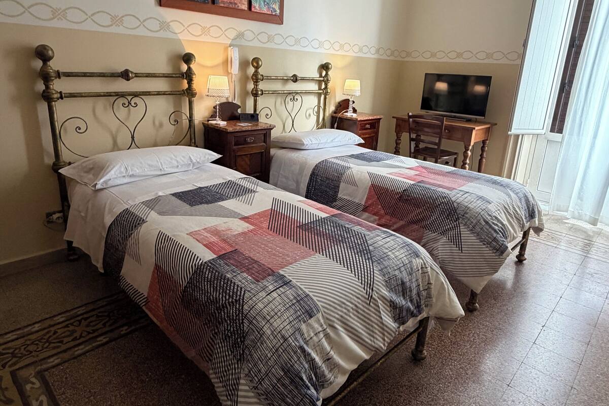 A bedroom with two beds, a desk, a chair, a television, and a window.