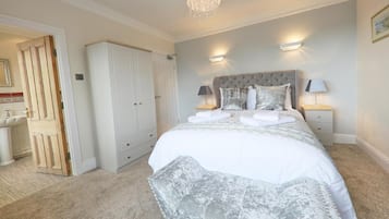 A bedroom with a large bed, two bedside lamps, a wardrobe, and a chandelier.