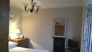 A bedroom with a bed, a dresser, a television, a mirror, and a fireplace. - Llwyn Country House (Llanelli)