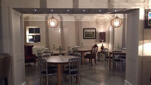A dining area with multiple round tables and chairs, pendant lighting, and a framed picture on the wall. - Llwyn Country House (Llanelli)