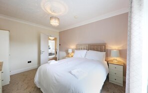A bedroom with a large bed, bedside tables with lamps, a door leading to another room, and a ceiling light fixture. - Llwyn Country House (Llanelli)