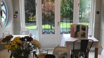A dining area with a table set for two, featuring a vase of flowers, a bowl of fruit, and a glass of orange juice.
