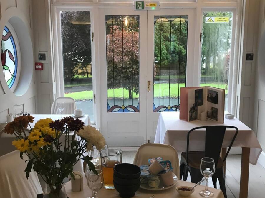 A dining area with a table set for two, featuring a vase of flowers, a bowl of fruit, and a glass of orange juice.