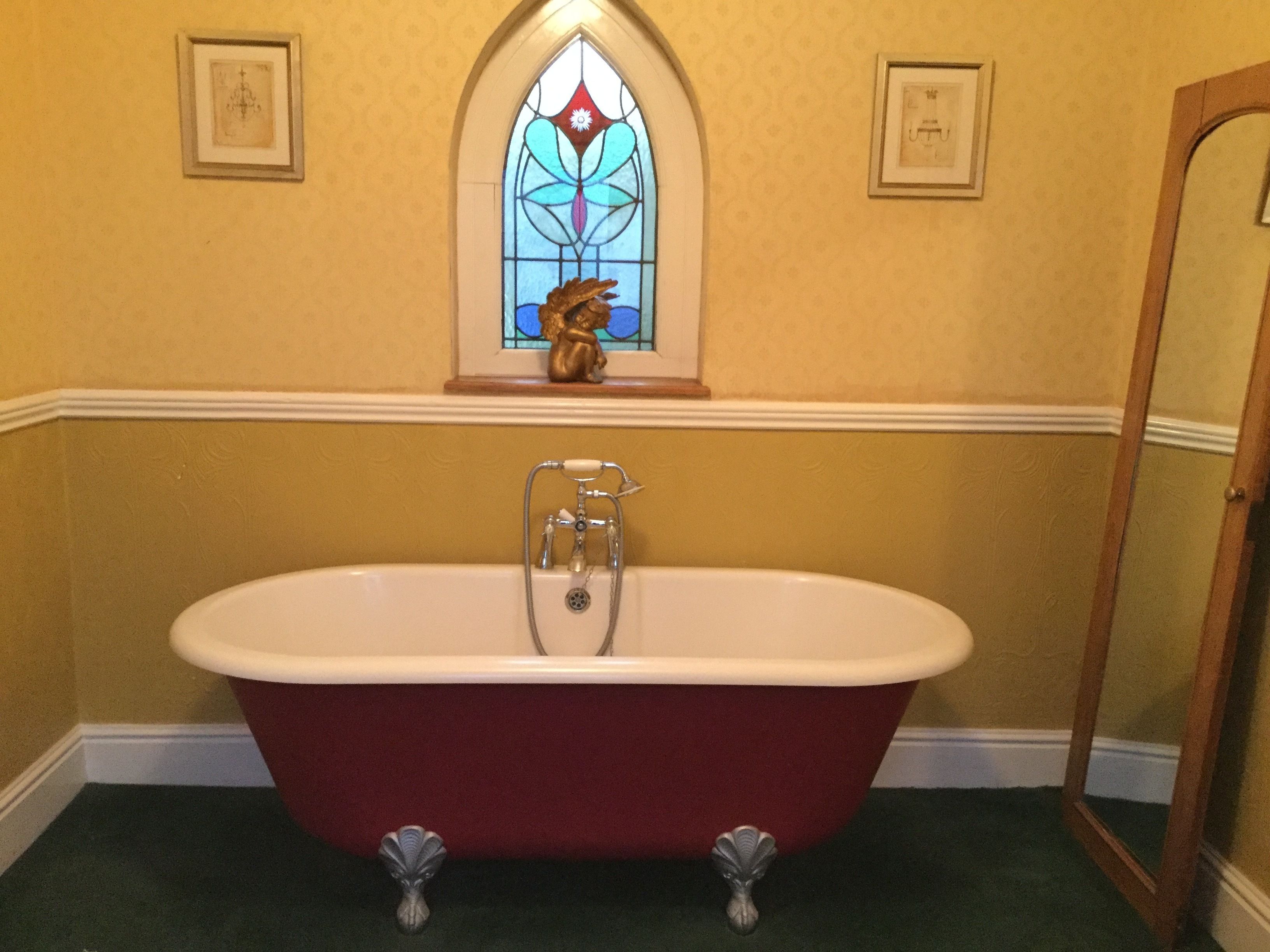 A bathroom with a freestanding bathtub, a stained glass window, and framed pictures on the walls.