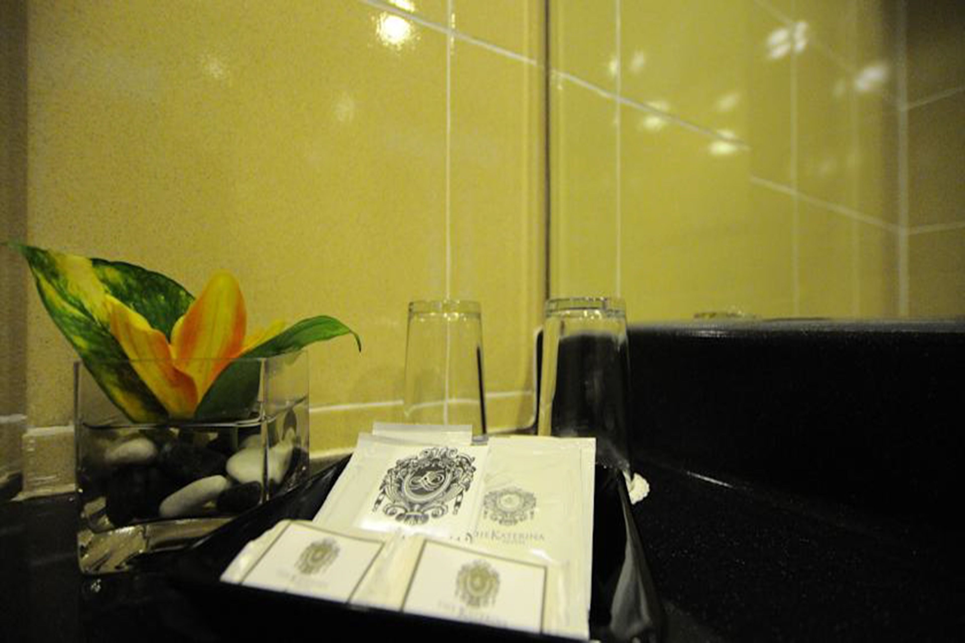 Casa de banho com um vaso de flores, um copo de água e um tabuleiro com uma toalha e um pequeno objeto.