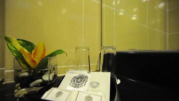 Casa de banho com um vaso de flores, um copo de água e um tabuleiro com uma toalha e um pequeno objeto.