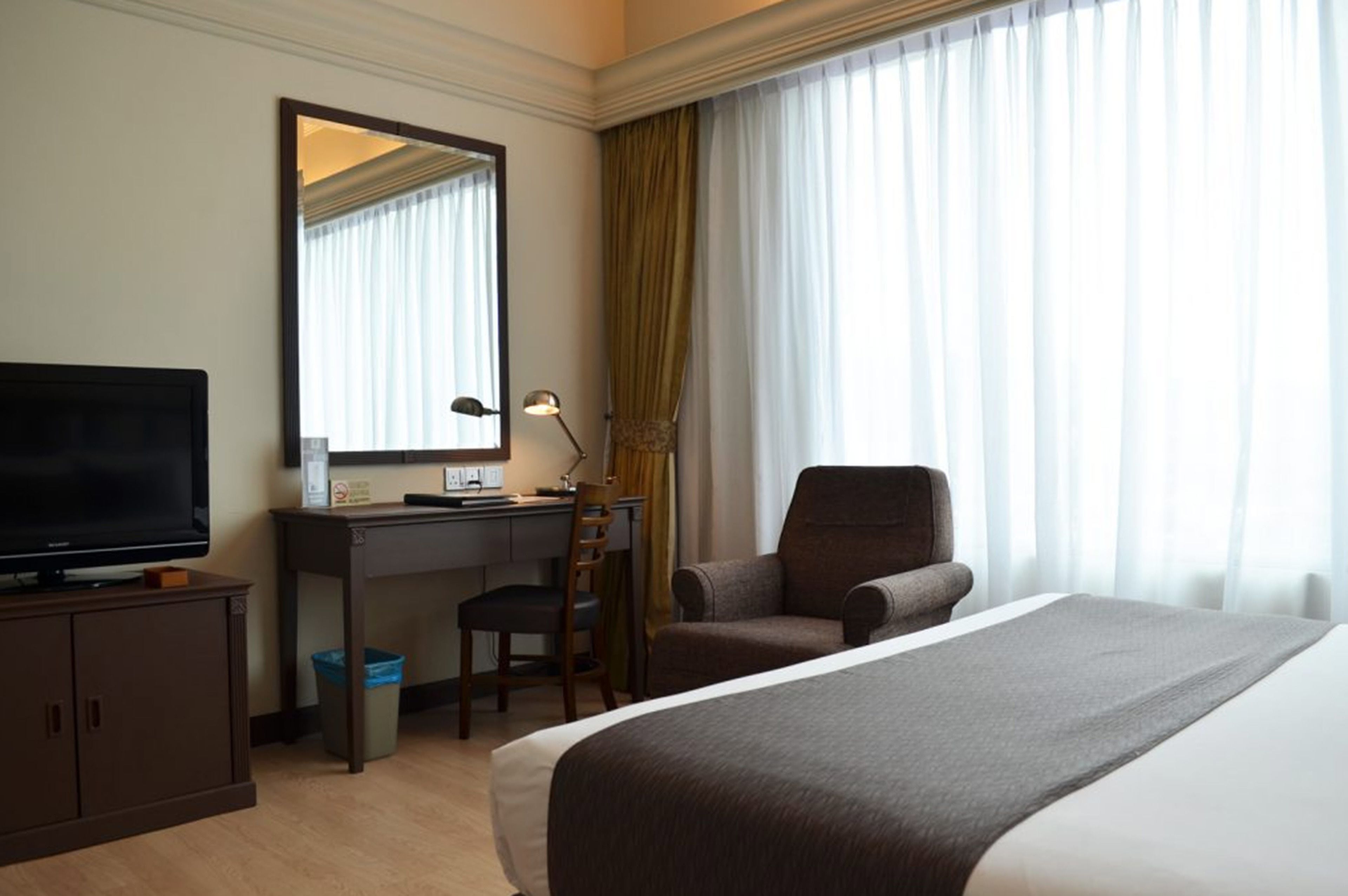 A hotel room with a bed, a desk with a chair, a television, and a large window with curtains.