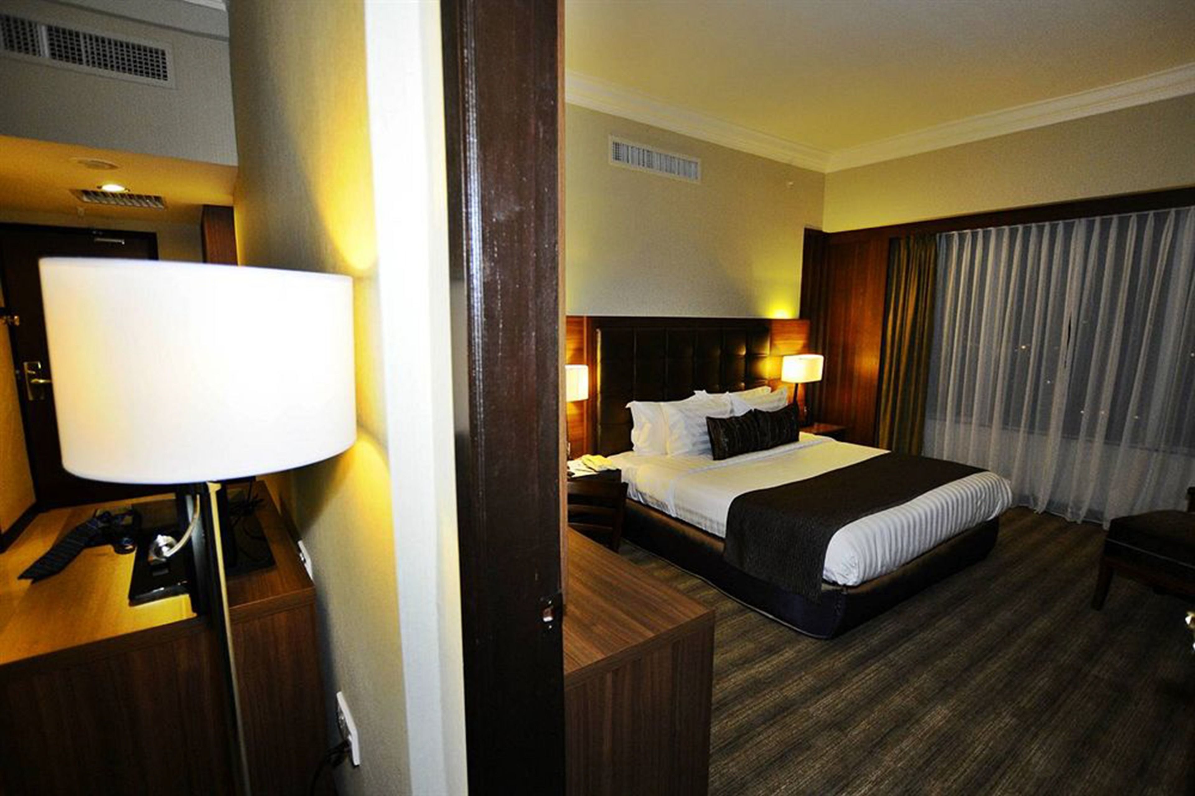 A hotel room with a bed, bedside lamps, a desk, and a chair.