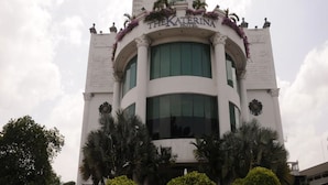 Un hotel con un cartel llamativo, una entrada principal y jardines simétricos con palmeras.