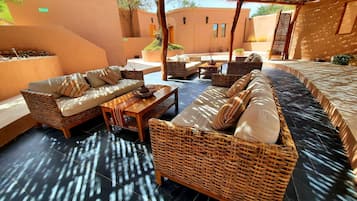 Un área de estar al aire libre con mobiliario de mimbre, piso de baldosas y techo de paja.