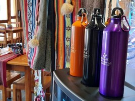 Una mesa con tres botellas de agua y una manta tejida de colores.