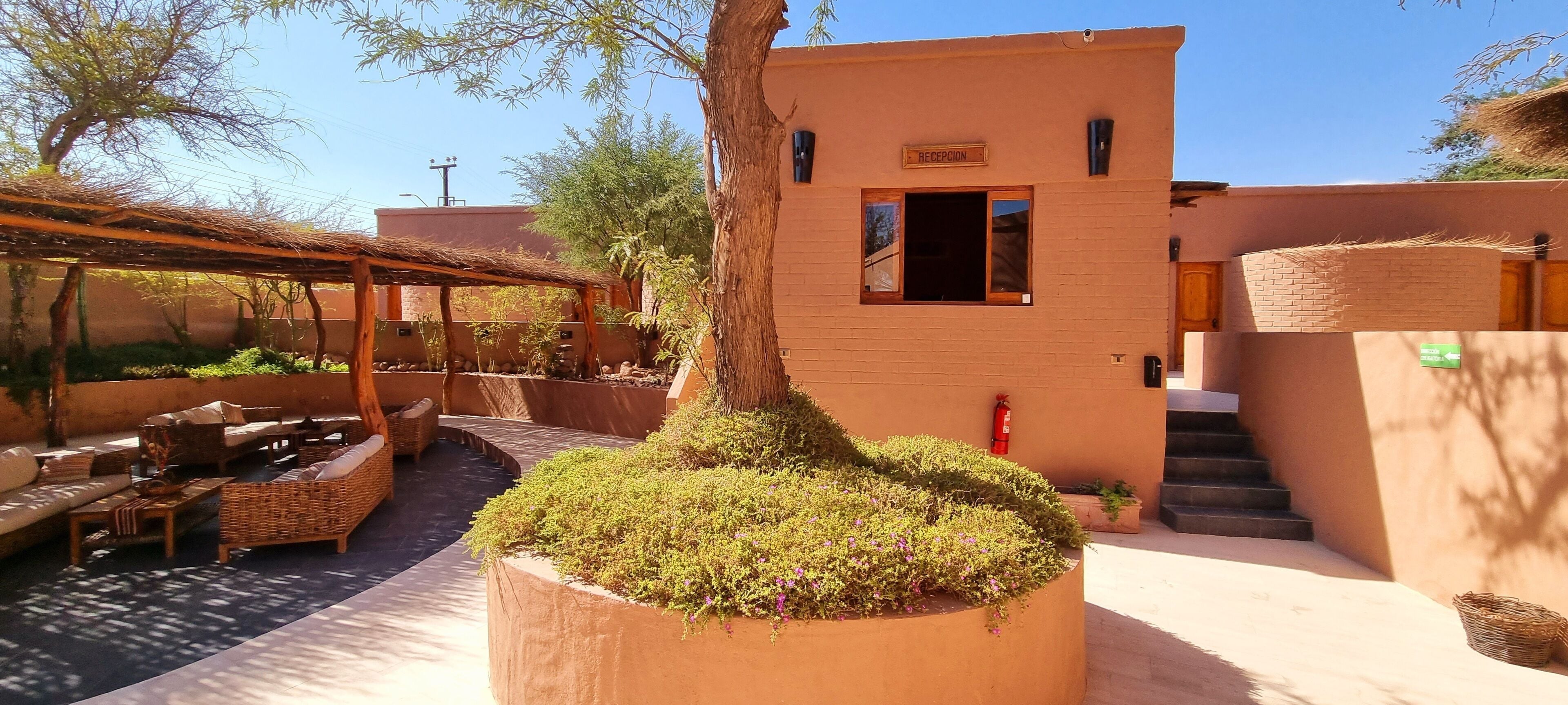 A reception area with a wooden pergola, outdoor seating, and a large planter with greenery.