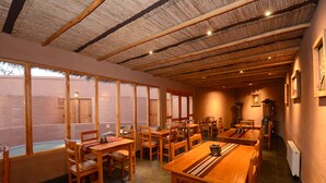 Un restaurant avec des tables et des chaises en bois, de grandes fenêtres et un plafond recouvert de chaume.