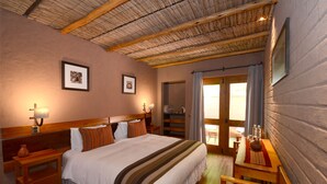 Une chambre avec un grand lit, une tête de lit en bois, des tables de chevet, une petite table avec un vase, et une vue sur l’extérieur par une porte.