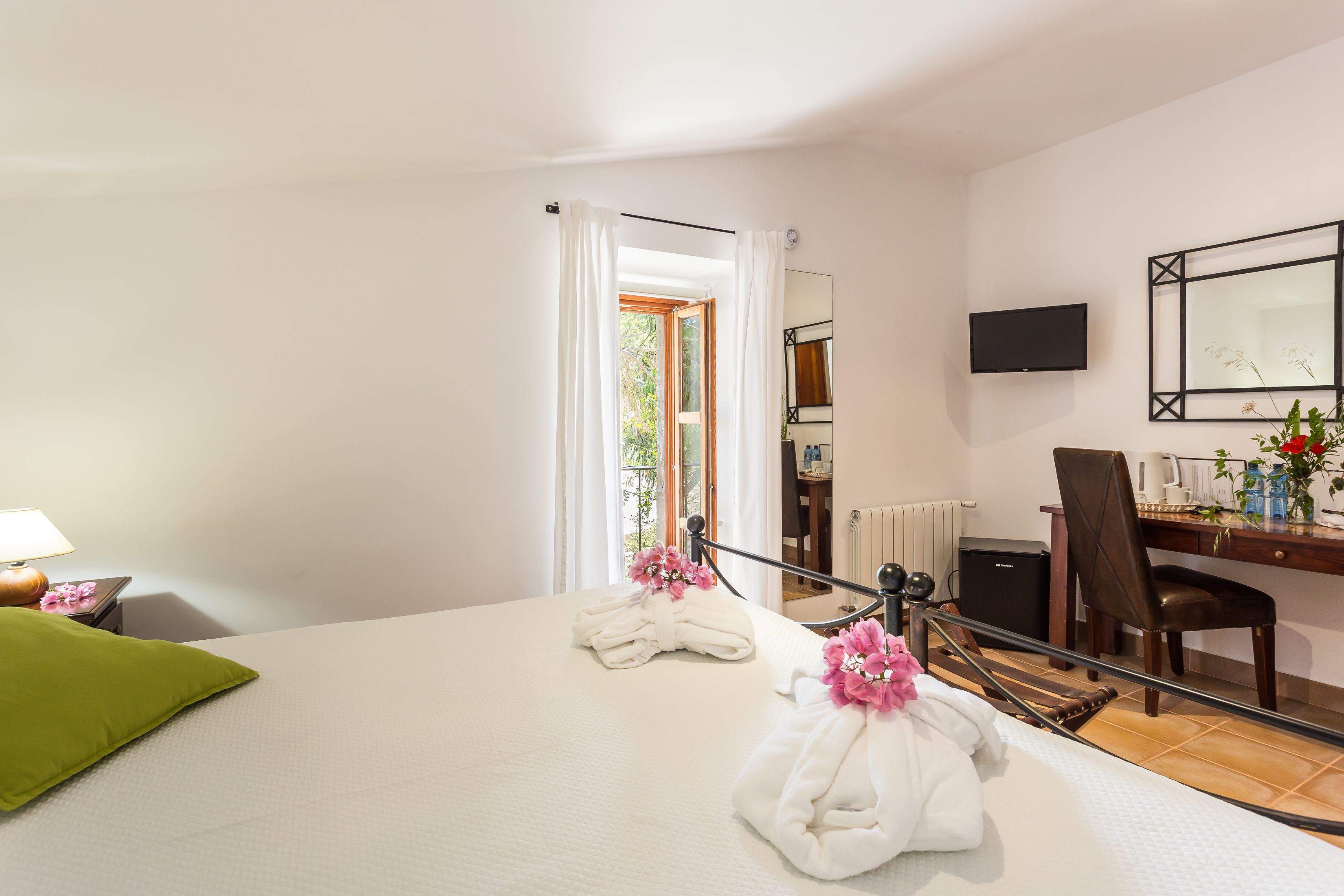 Habitación de hotel con cama, escritorio, silla, televisión y ventana con cortinas.