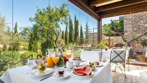 Une table de petit-déjeuner installée à l’extérieur, avec vue sur des arbres et un mur de pierres.
