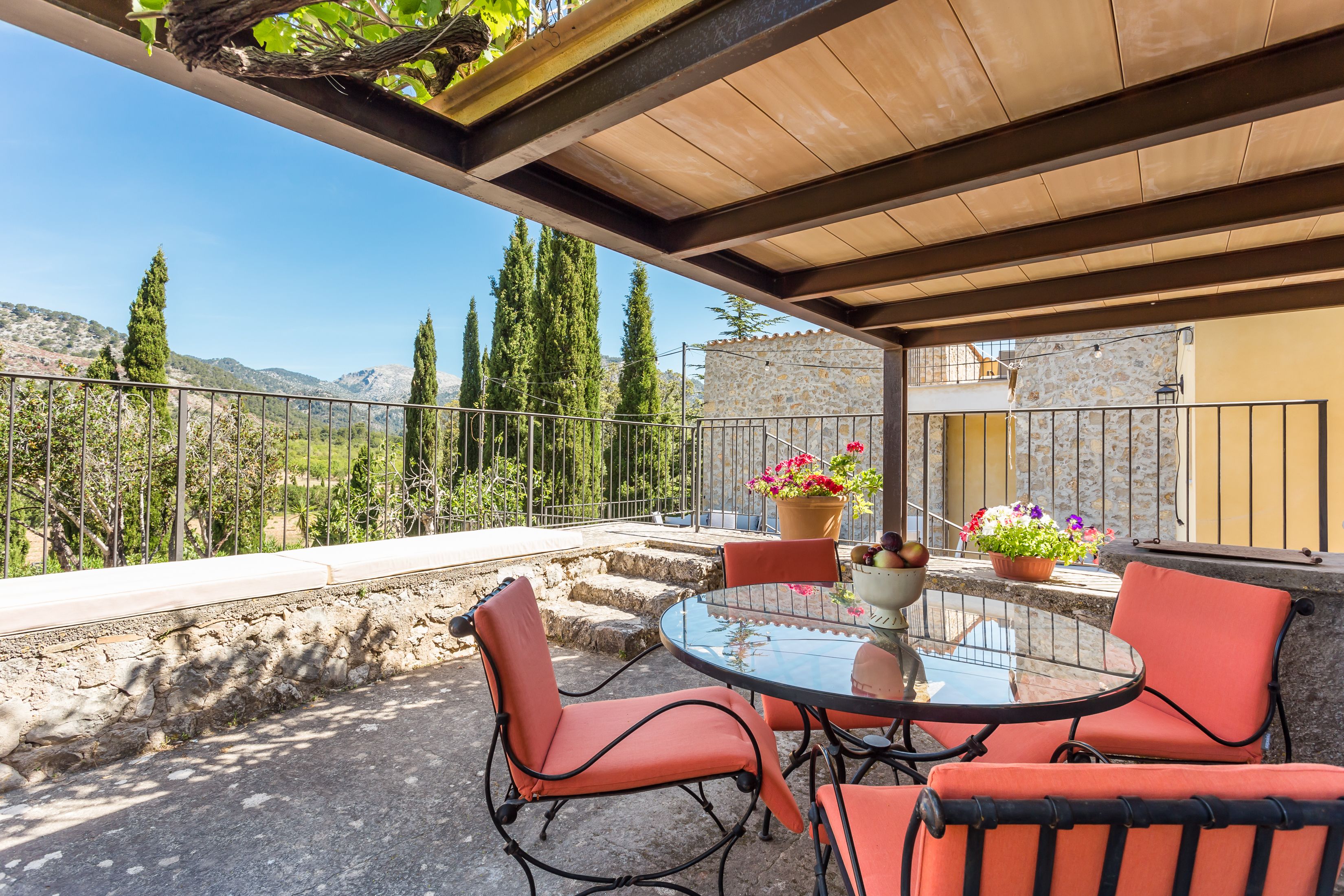 A covered outdoor seating area with a table and chairs, potted plants, and a view of mountains.