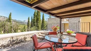 A covered outdoor seating area with a table and chairs, potted plants, and a view of mountains.