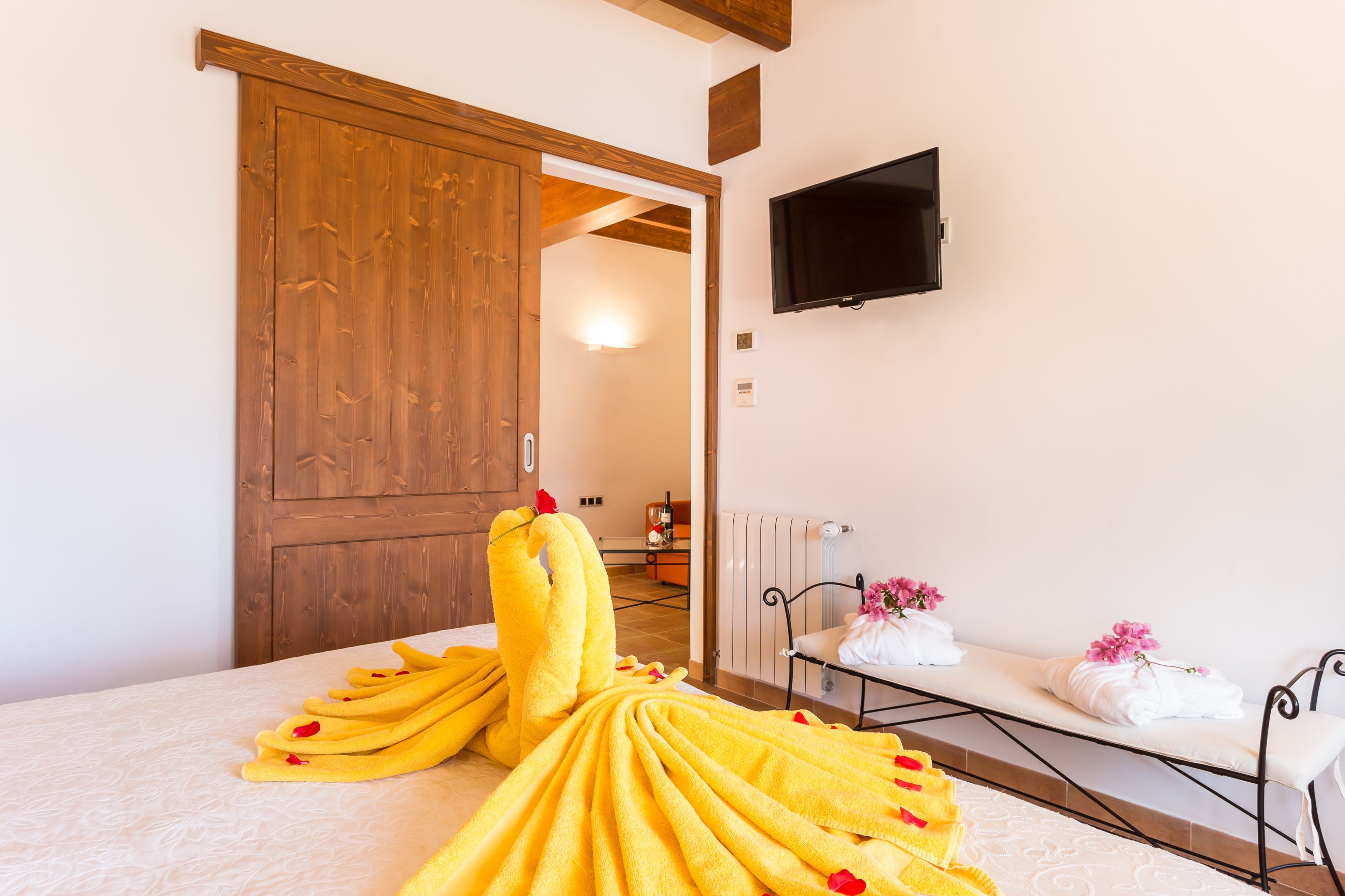 Een kamer met een bed, een houten deur, een televisie en een bank met handdoeken en bloemen.