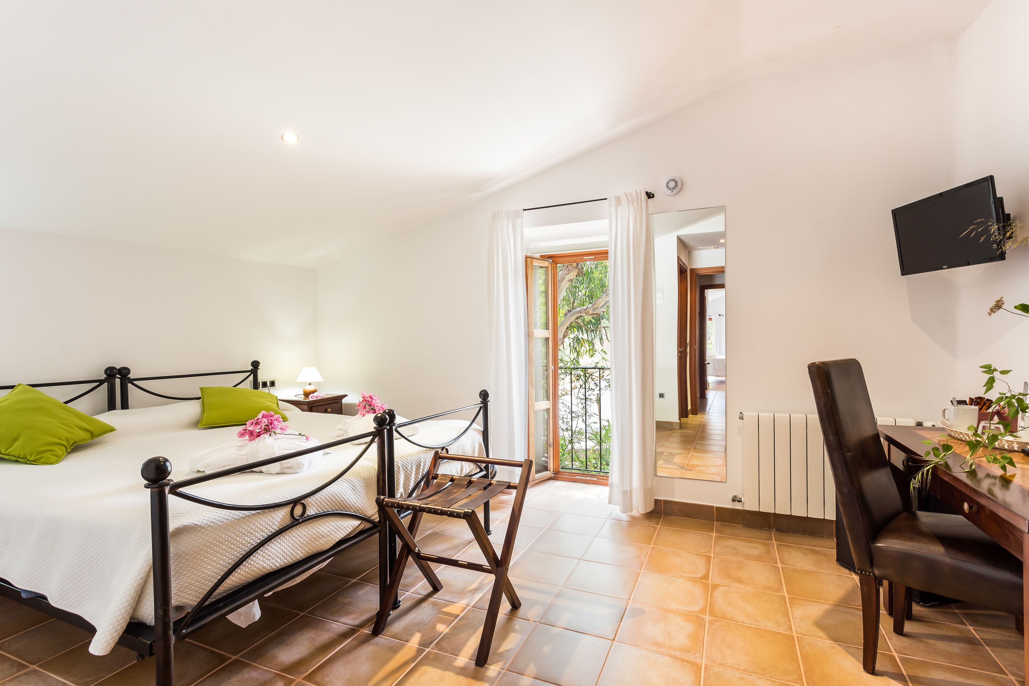A bedroom with a bed, a desk, and a chair. There is a window with curtains, a TV mounted on the wall, and a radiator.