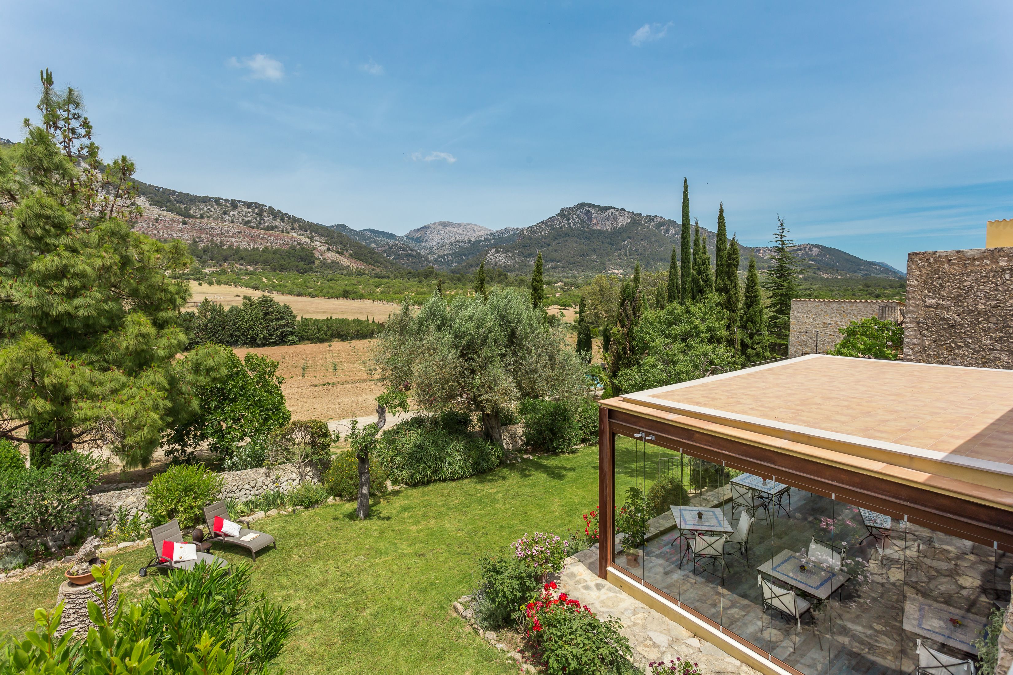 A terrace with outdoor furniture, a stone wall, and a view of a mountainous landscape.