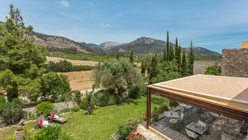 A terrace with outdoor furniture, a stone wall, and a view of a mountainous landscape.
