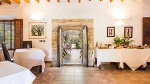 Un espace repas agrémenté d’une arche en pierre menant à un patio extérieur, de nappes blanches et d’une variété de plats disposés sur la table.