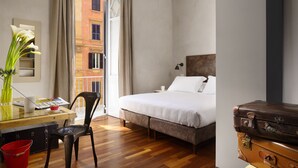 A hotel room with a bed, a desk with a chair, a vase with flowers, and a suitcase. - San Pietro Boutique Rooms (Rome)