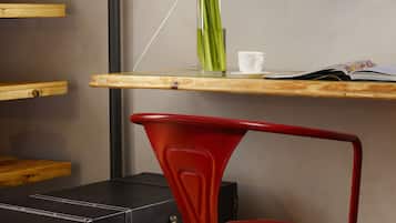 Een kamer met een houten plank, een rode stoel, een zwarte koffer, een vaas met bloemen, een beker en een flatscreen-televisie.