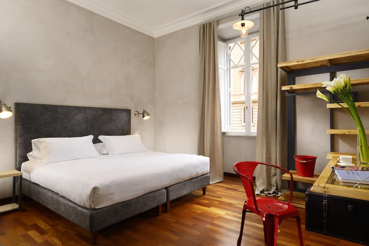 Une chambre d’hôtel bien rangée, avec un lit, un bureau, une chaise et une fenêtre avec des rideaux.