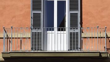 A building facade with a balcony, a wooden door with a decorative metal grille, and a window with shutters.