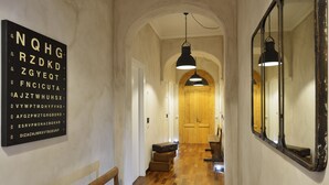 A hallway with wooden flooring, a bench, a wall-mounted mirror, and a ceiling light fixture. - San Pietro Boutique Rooms (Rome)