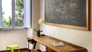 A classroom with a chalkboard listing room names and times, a wooden desk, and colorful stools. - San Pietro Boutique Rooms (Rome)