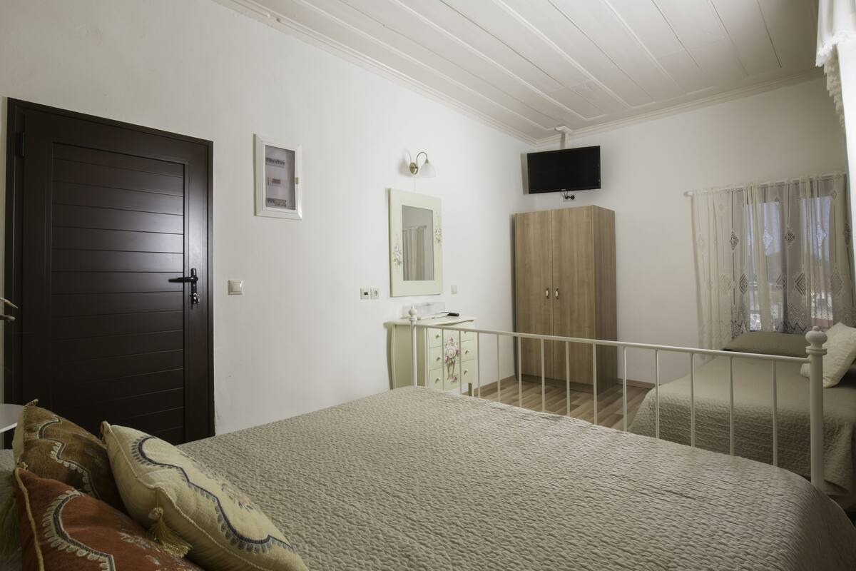Un dormitorio con cama, armario, espejo, televisión y ventana con cortinas.