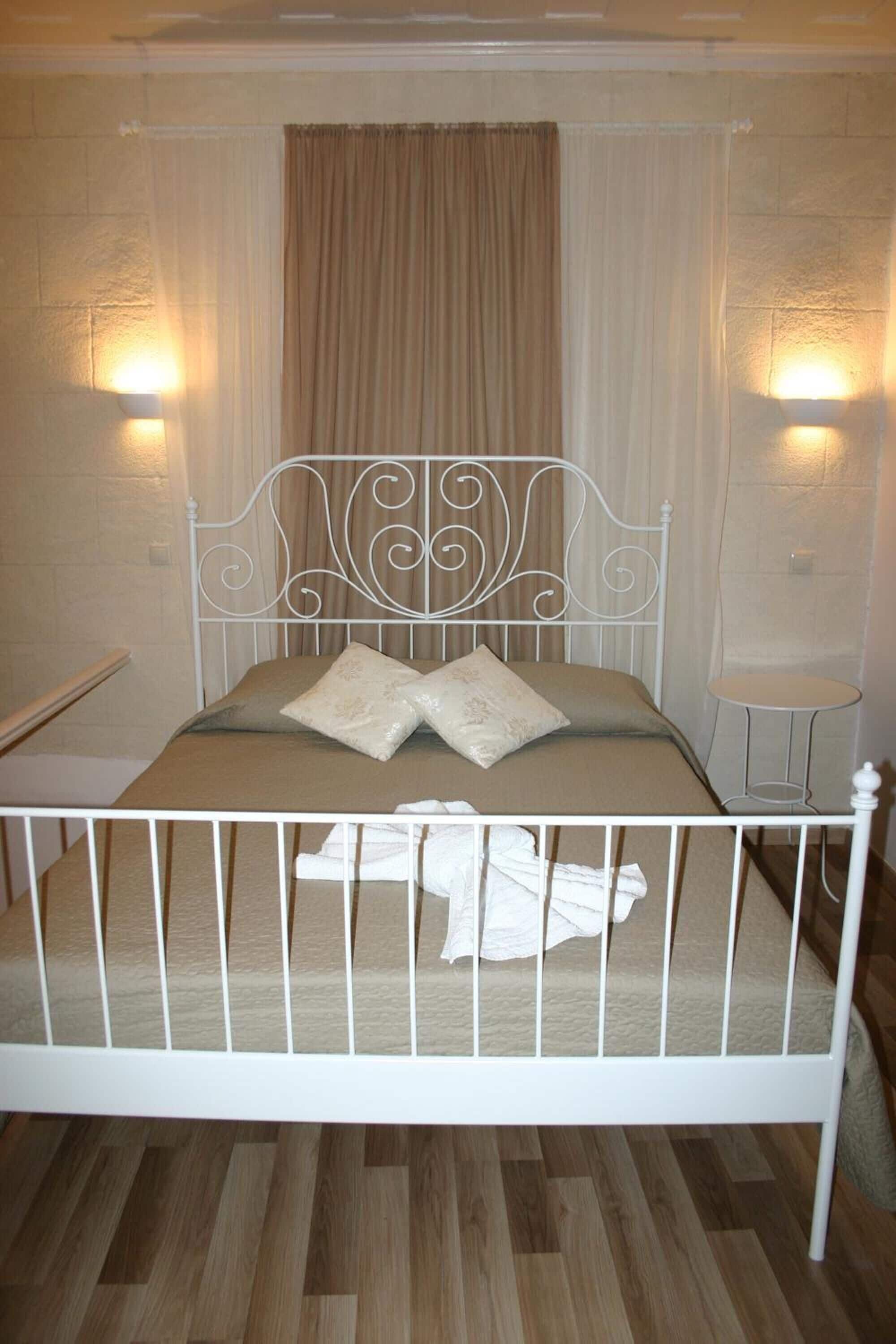 A bed with a white metal frame, beige bedding, and two pillows. There is a small round table beside the bed.
