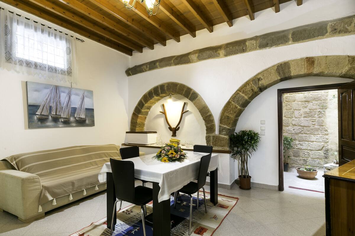 Un comedor con una mesa preparada para cuatro personas, rodeada de sillas, un sofá y una planta en maceta.