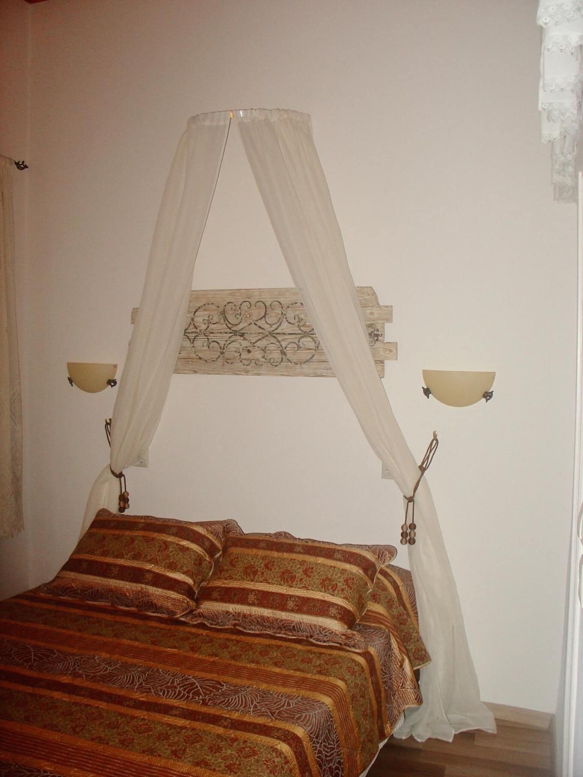 Una cama con dosel, dos lámparas fijadas a la pared y un adorno decorativo sobre la cama.