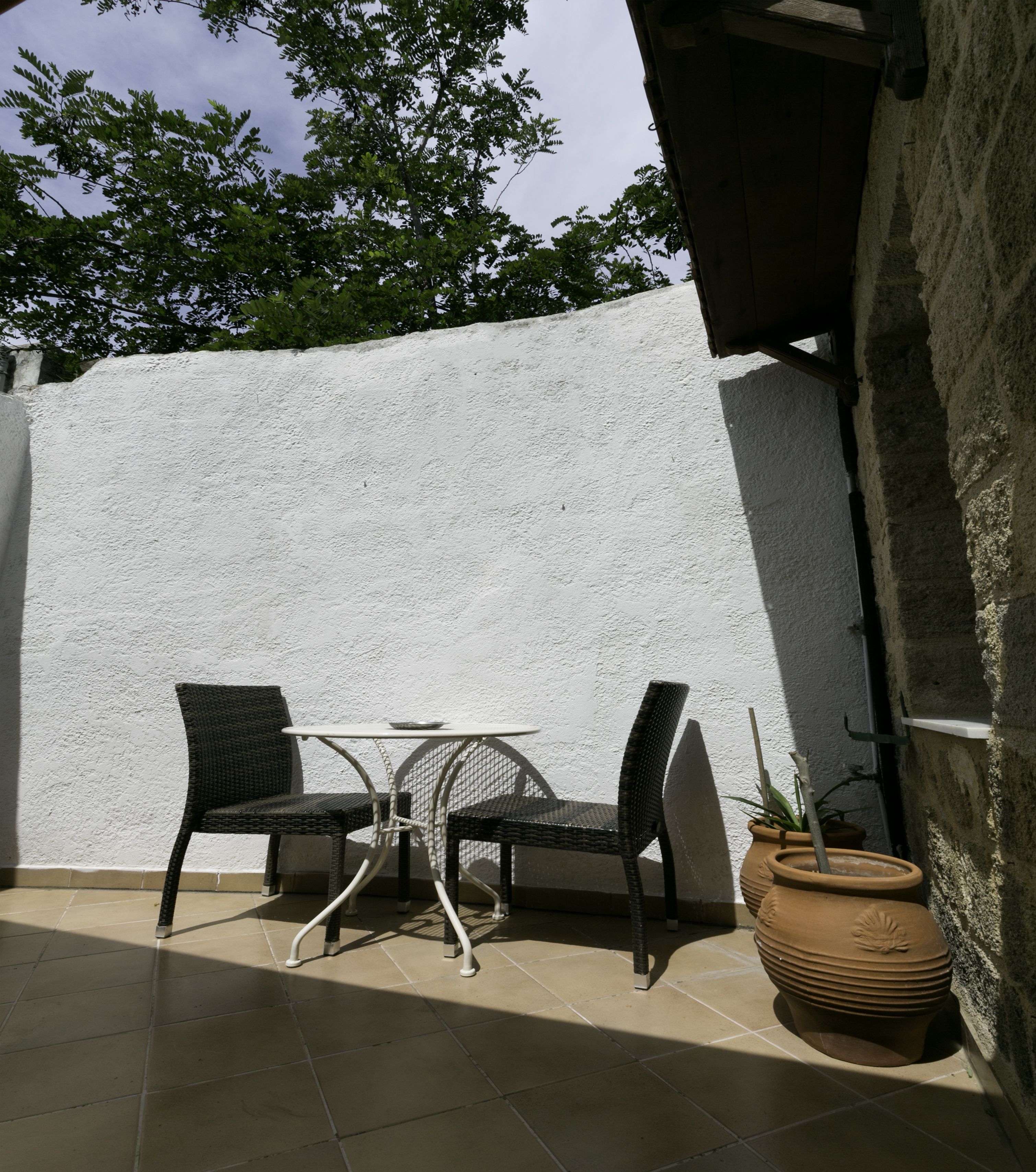 An outdoor patio with two wicker chairs and a small round table, a potted plant, and a white textured wall.