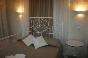 A bed with a metal headboard, two pillows, a small round table, and a wall-mounted light fixture.