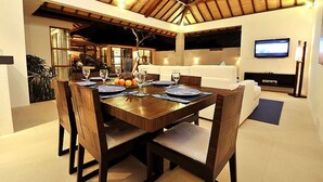 A dining area with a wooden table set for four, surrounded by cushioned chairs. - Arama Riverside (Legian)
