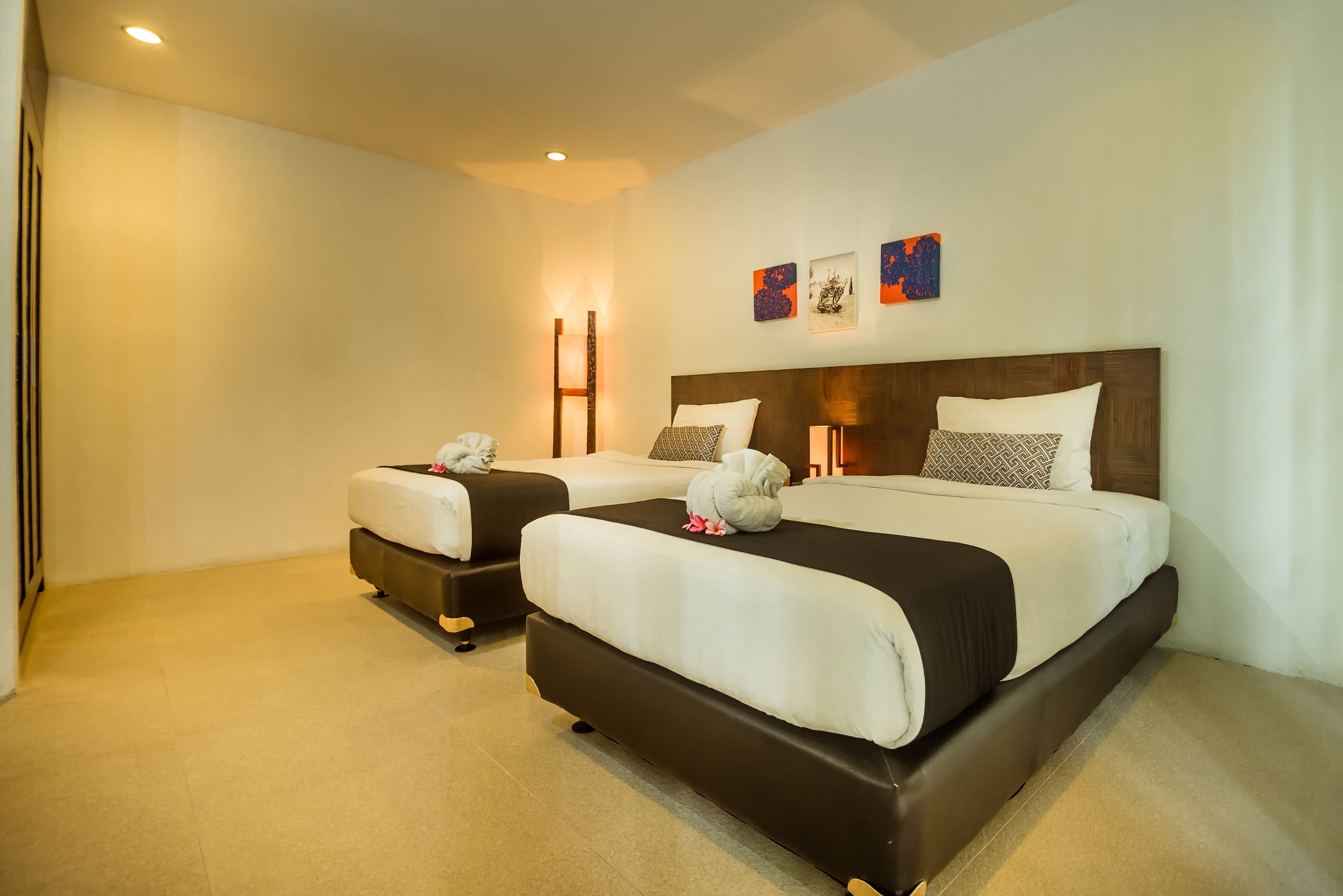 A hotel room with two beds, a bedside table with a lamp, and artwork on the wall.