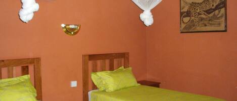 A hotel room with two beds, each with a green bedspread and matching pillows. There is a wall-mounted air conditioner and a decorative piece above the beds.