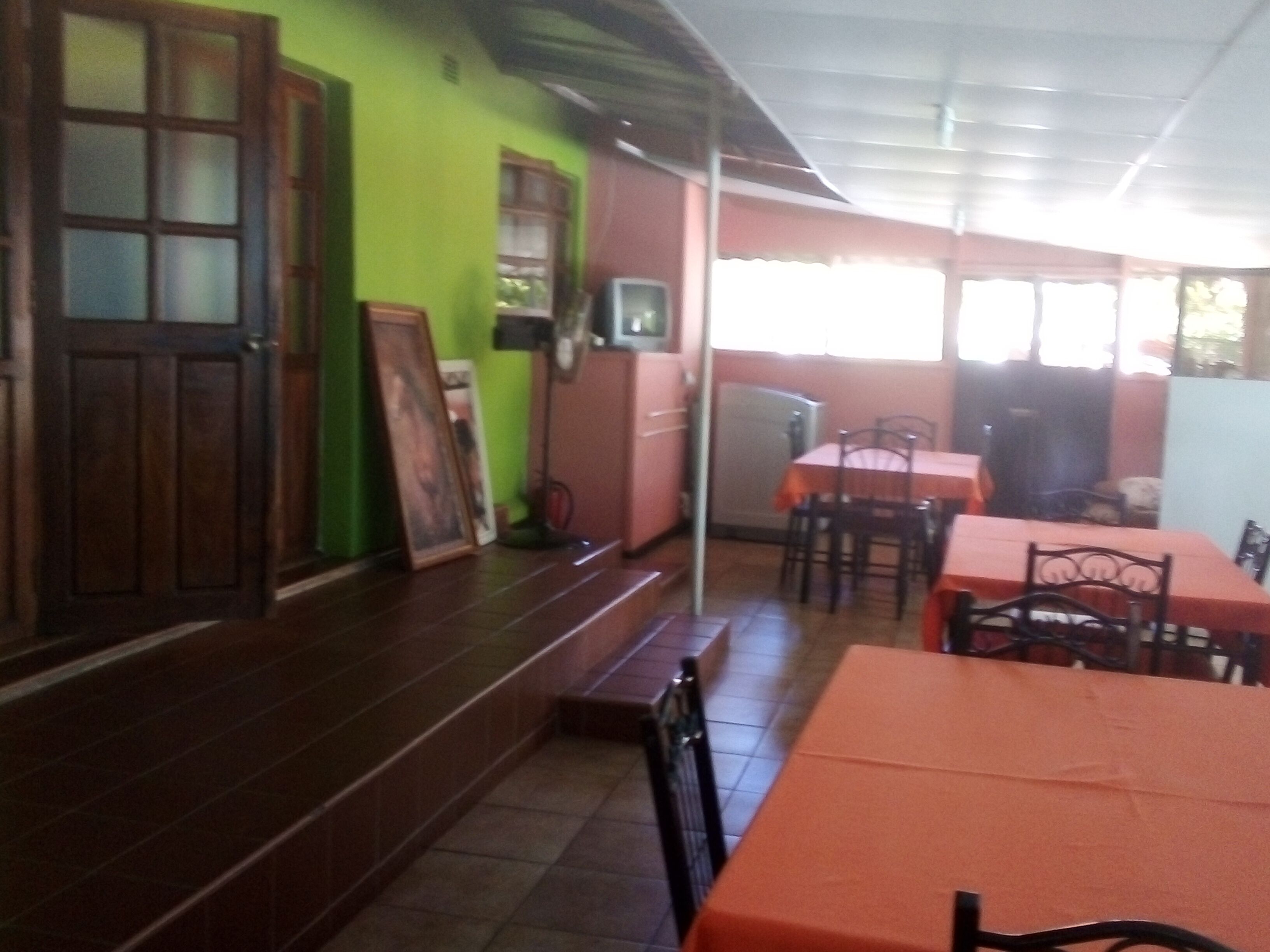 Un restaurant doté d’un mur végétal, d’une porte en bois et d’un sol carrelé. On y trouve des tables et des chaises, ainsi qu’une fenêtre avec des rideaux.