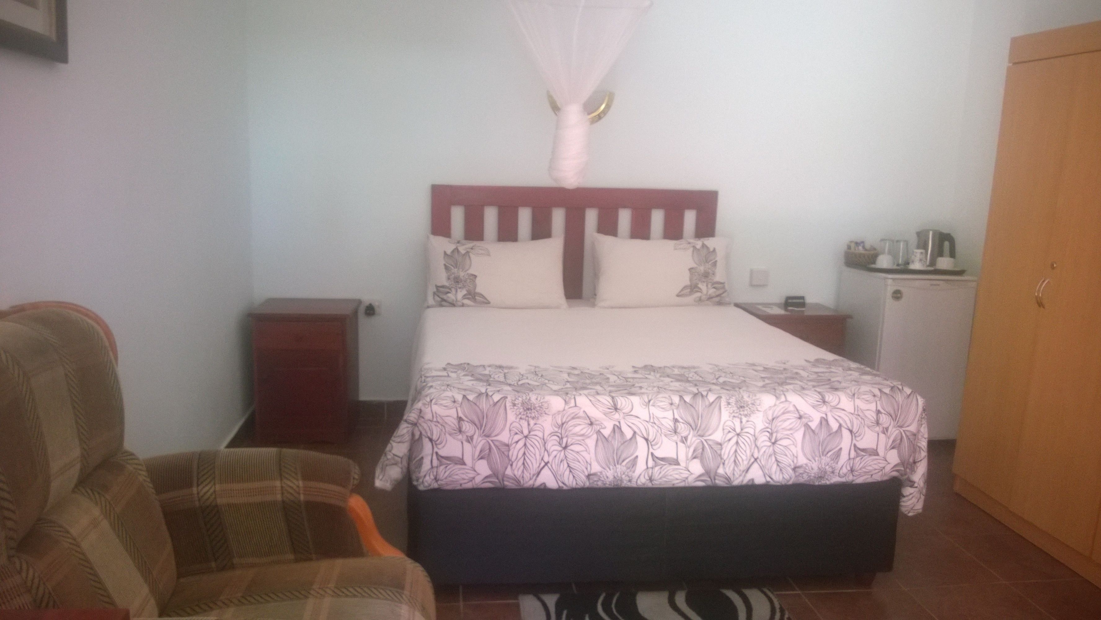 Un dormitorio con cama, mesita de noche, silla, armario y una pequeña cocina.