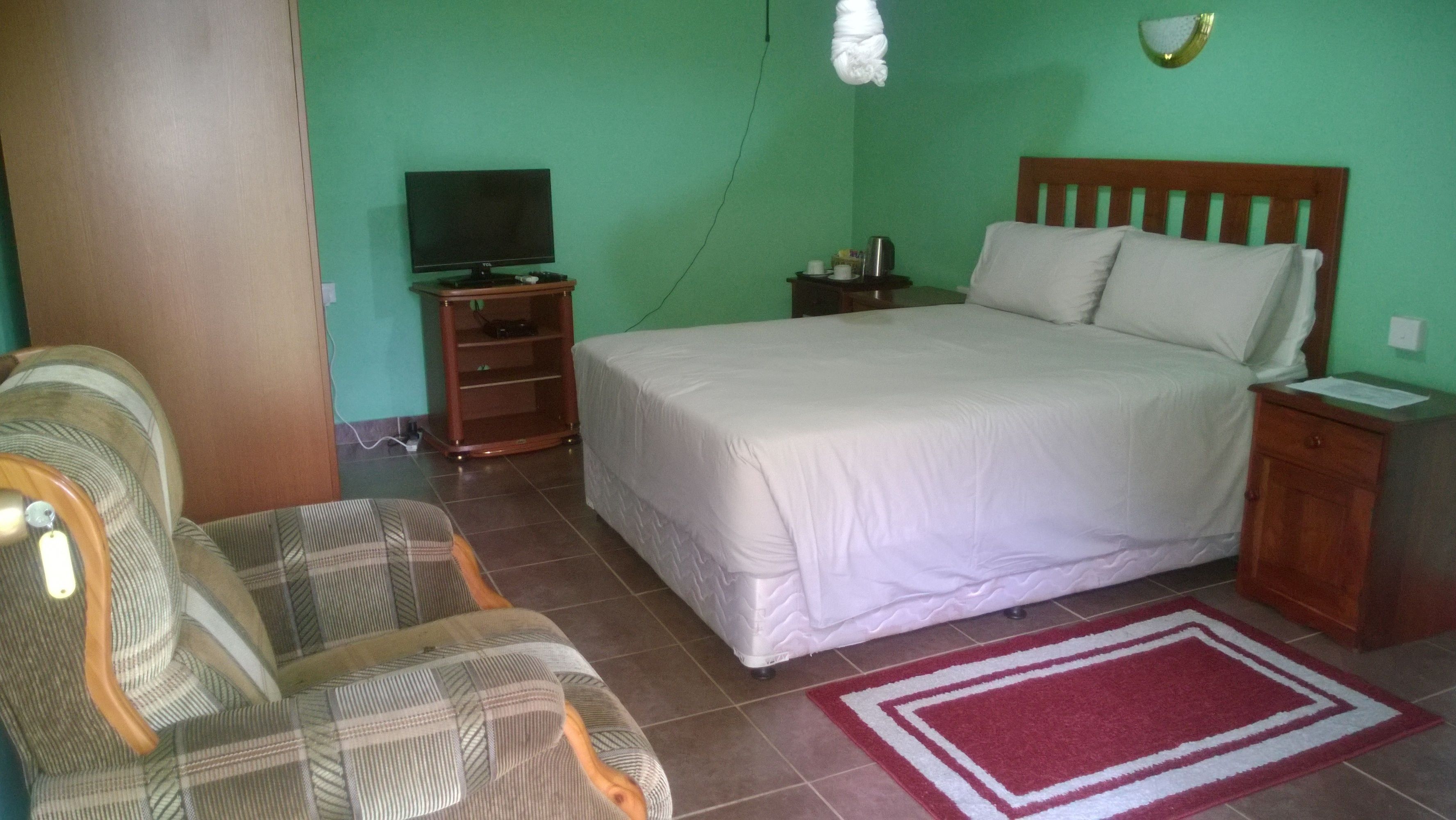 Un dormitorio con cama, sillón, televisor y mesita de noche.