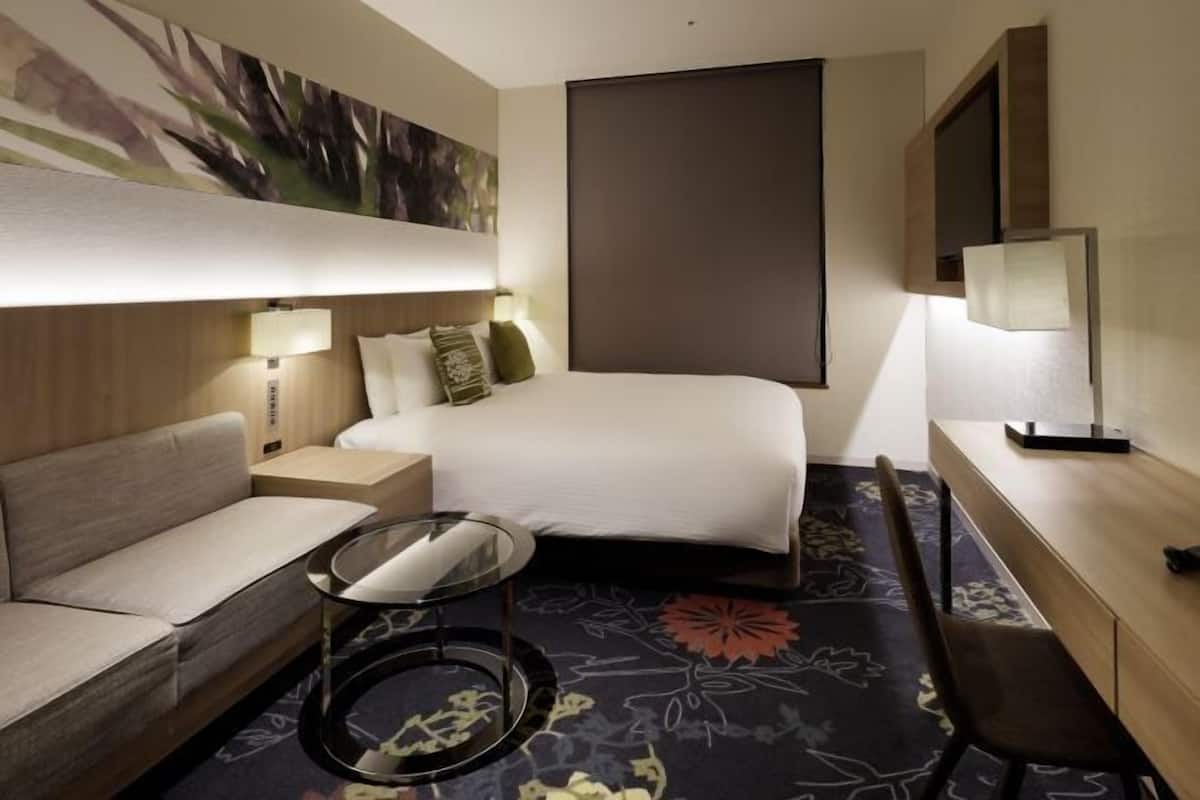A hotel room with a bed, a sofa, a small table, and a desk.